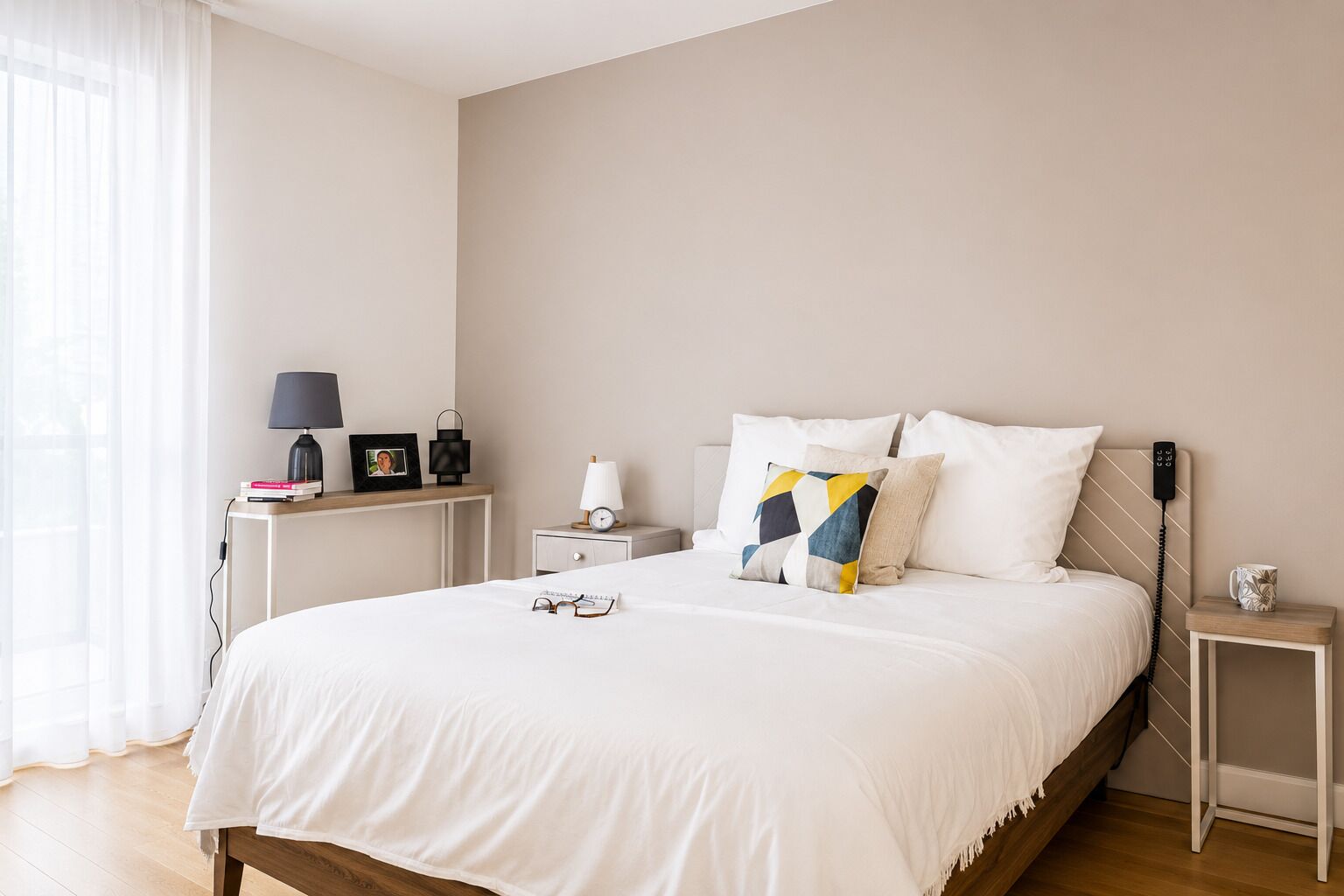 A neatly arranged bedroom with a bed, bedside tables, a lamp, a clock, and a bedside phone.