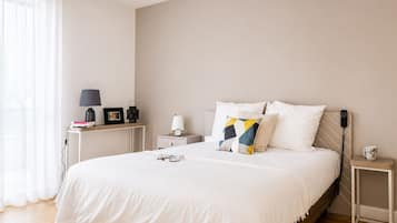 A neatly arranged bedroom with a bed, bedside tables, a lamp, a clock, and a bedside phone.