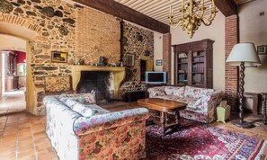 A stone-walled room with a fireplace, floral-patterned sofas, a wooden coffee table, and a patterned rug.