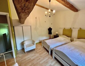 A bedroom with two beds, a chair, a chandelier, and a wardrobe.