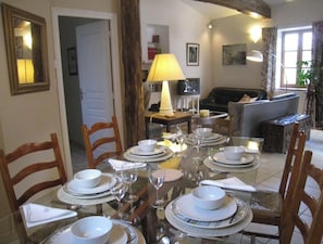A dining area with a table set for four, chairs, a lamp, and a sofa in the background.