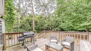 Eine Holzterrasse mit Gartenmöbeln, einem Grill und Blick auf ein bewaldetes Gebiet.