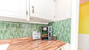 Eine Küche mit Kaffeemaschine, einem Schild mit der Aufschrift 'COFFEE TIME' und einer grünen, gefliesten Spritzschutzwand.