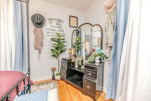 Un dormitorio con cama, cómoda, espejo, reloj de pared y un cartel con los horarios de visita.