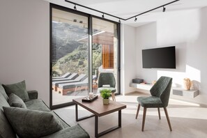 A modern living room with a large sliding glass door, a flat-screen TV, a green sofa, a wooden coffee table, and a green armchair.