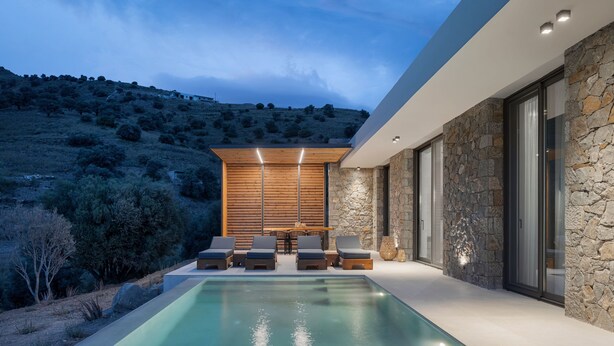 Zona de piscina exterior moderna amb gandules, una taula de dinar i una paret de pedra.