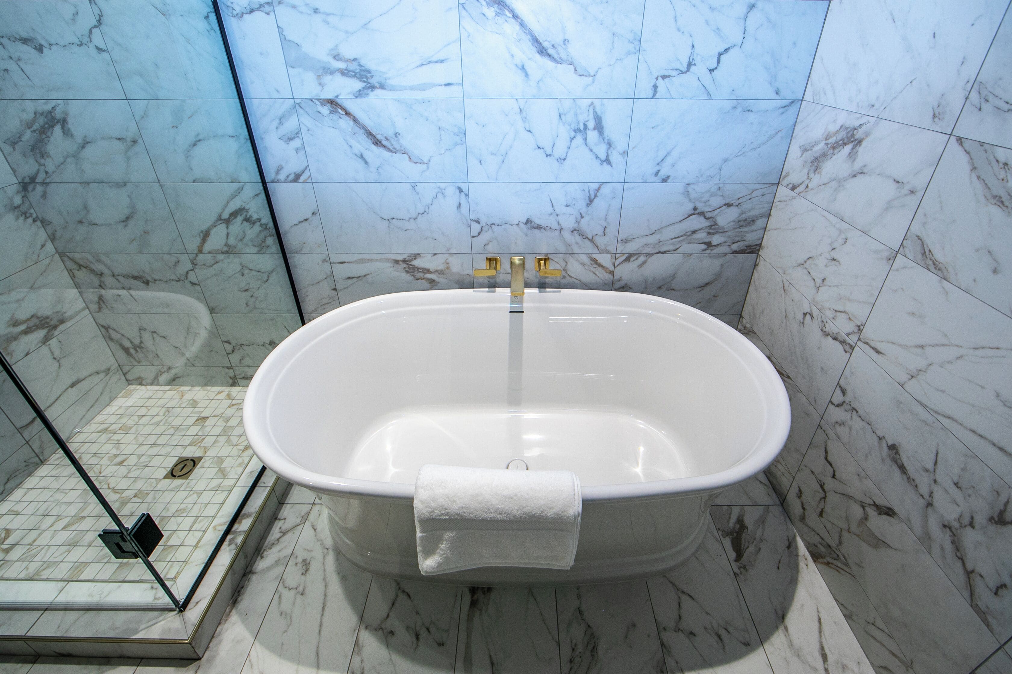 A bathroom with a freestanding bathtub, a glass shower enclosure, and marble walls.