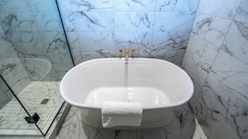 A bathroom with a freestanding bathtub, a glass shower enclosure, and marble walls.