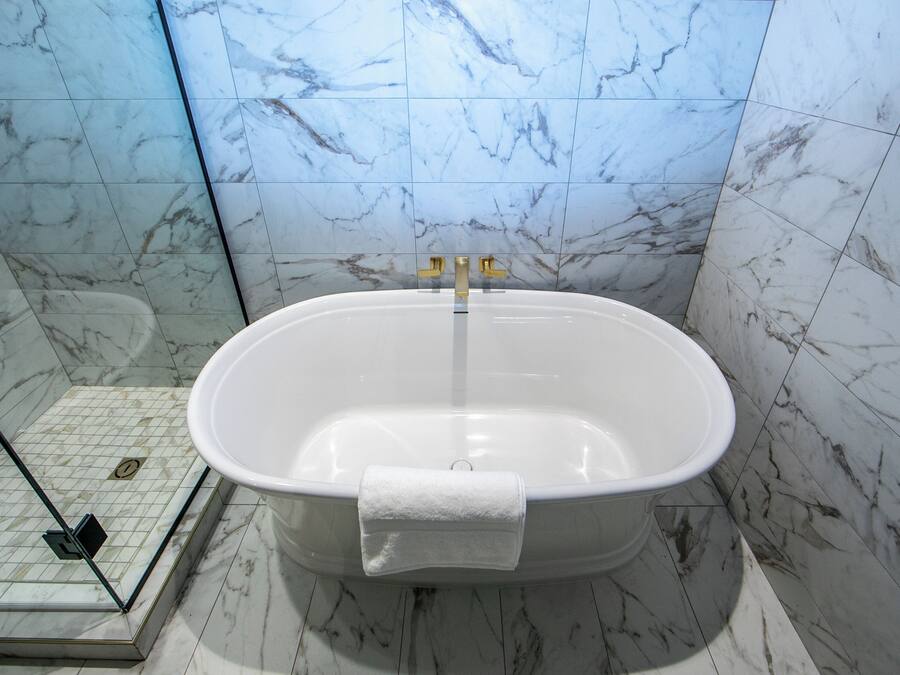 A bathroom with a freestanding bathtub, a glass shower enclosure, and marble walls.