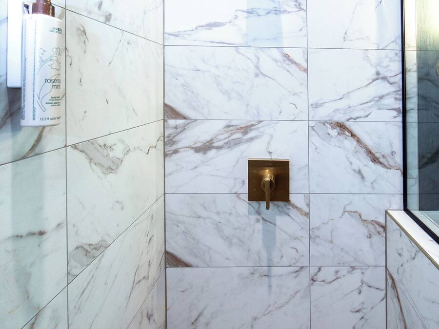 Baño con paredes de mármol, zona de ducha y mampara de vidrio.