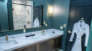 A bathroom with a double sink, a large mirror, and a robe hanging on the door.
