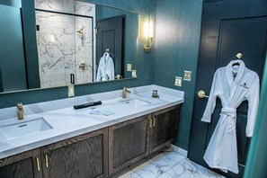 Une salle de bain avec un double vasque, un grand miroir et une robe accrochée à la porte.