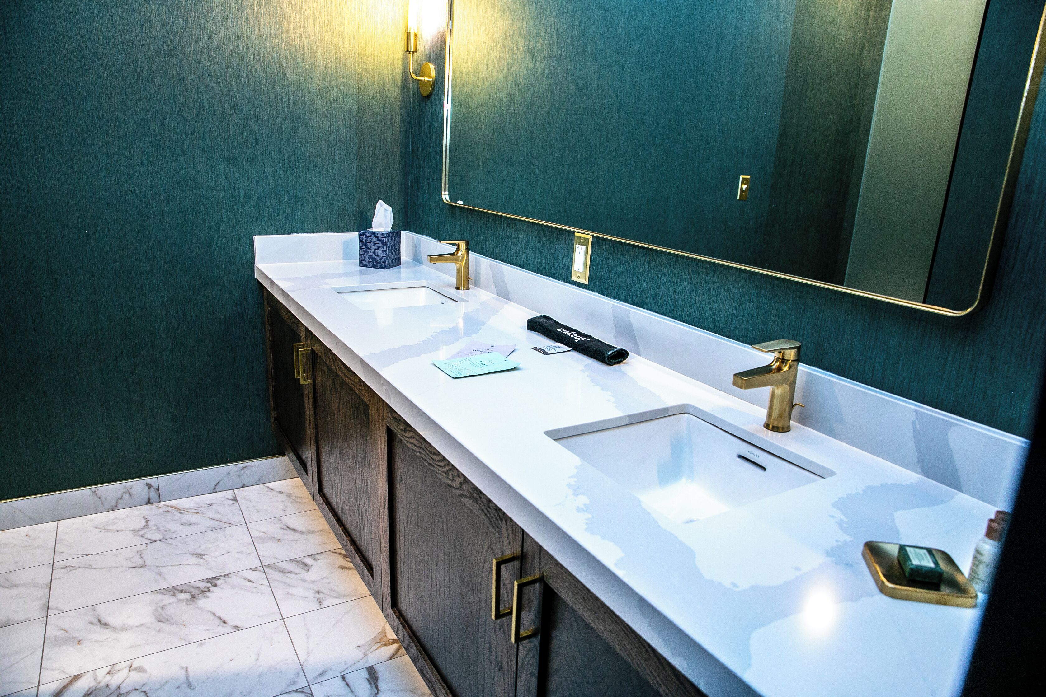 A bathroom with two sinks, a mirror, and a towel dispenser.
