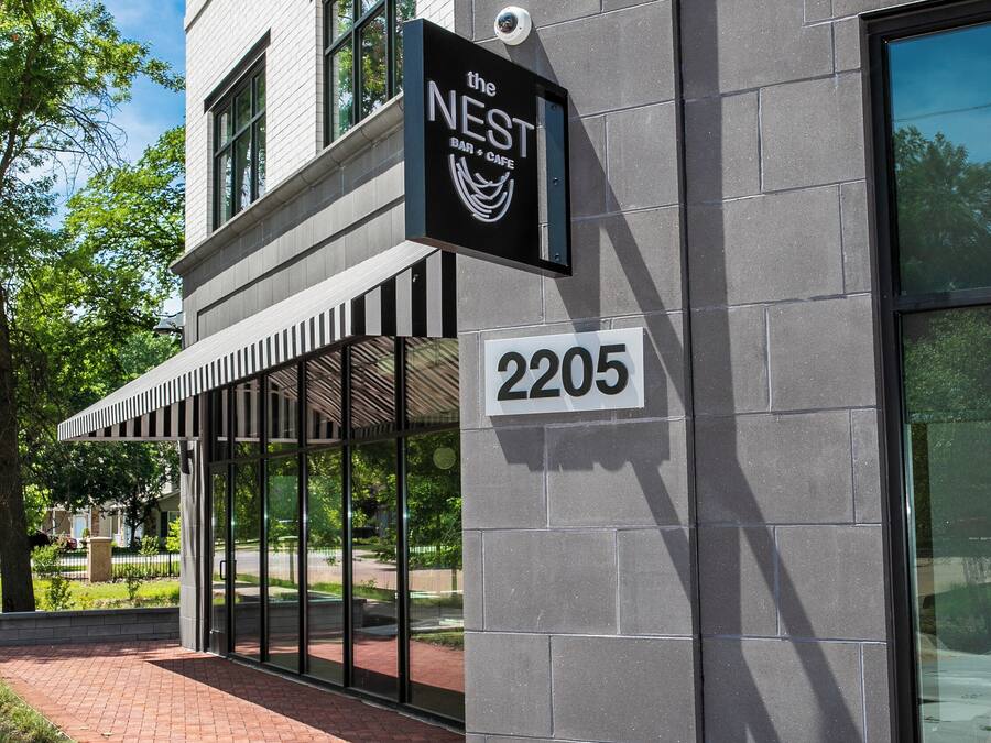 A building with a sign reading 'The Nest Bar & Cafe,' a brick pathway, and a large window.
