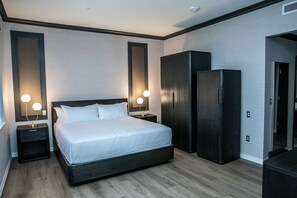 A modern bedroom with a large bed, two bedside tables with lamps, a wardrobe, and a mirror.