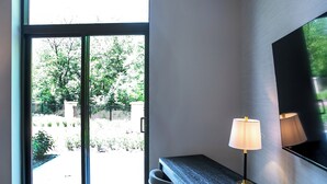 A room with a sliding glass door leading to a garden, a desk with a lamp, and a large mirror on the wall.