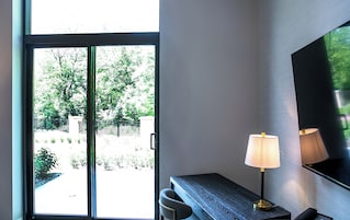 A room with a sliding glass door leading to a garden, a desk with a lamp, and a large mirror on the wall.