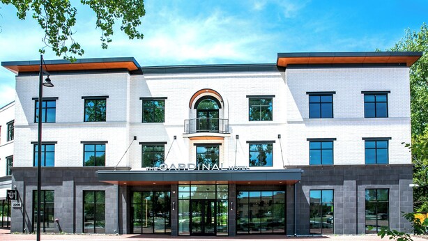 A modern hotel with a prominent arched entrance, large windows, and a sign reading 'The Cardinal Hotel.'