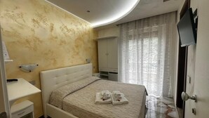 A modern bedroom with a large bed, a bedside table, a wardrobe, and a television. - CASA SÒL (Tropea)