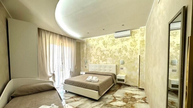 A modern hotel room with a large bed, a separate sofa, a vanity with a mirror, and a marble floor. - CASA SÒL (Tropea)