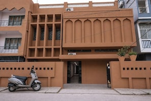 A building with a modern architectural style, featuring a prominent entrance with a gated driveway, a scooter parked in front, and a balcony with potted plants. - Hotel Subarnrekha Heritage (Ranchi)