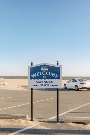 A welcome sign to Savannah Beach with a clear sky and a parked car in the background. - Quaint 2-bedroom, ground floor Condo with water views. Walk to downtown Lewes! (Lewes)