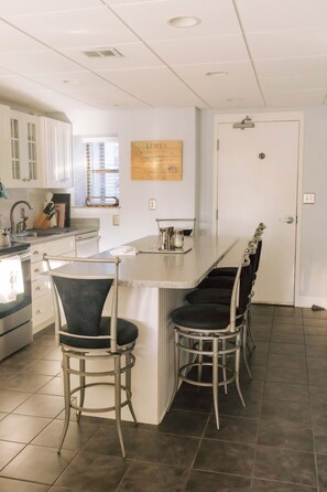 A kitchen with a bar area, white cabinets, a sink, and a door with a handle. - Quaint 2-bedroom, ground floor Condo with water views. Walk to downtown Lewes! (Lewes)