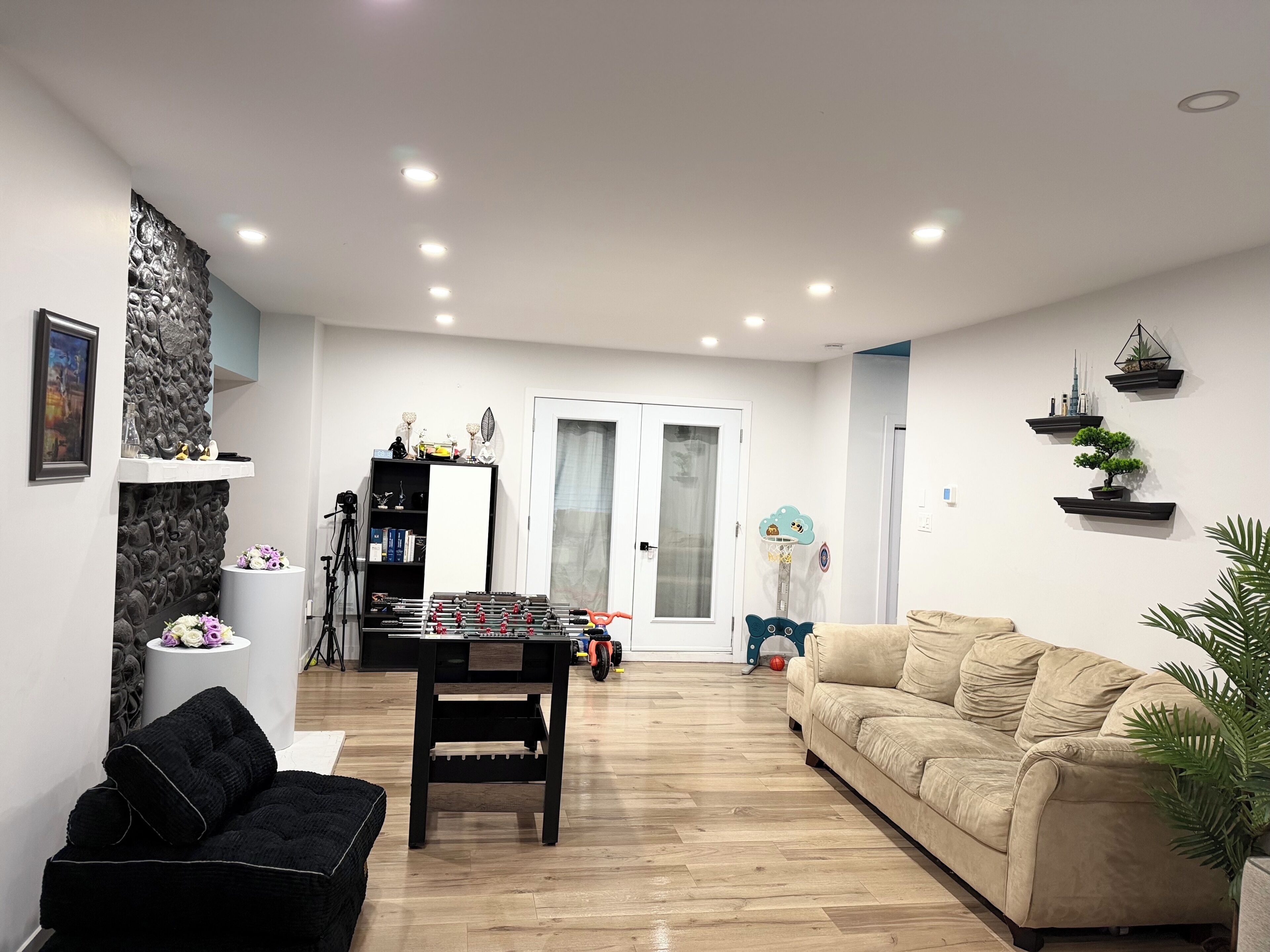 Una sala de estar con un sofá, un reposapiés negro, una mesa de centro de madera, una estantería y un estante montado en la pared con objetos decorativos.