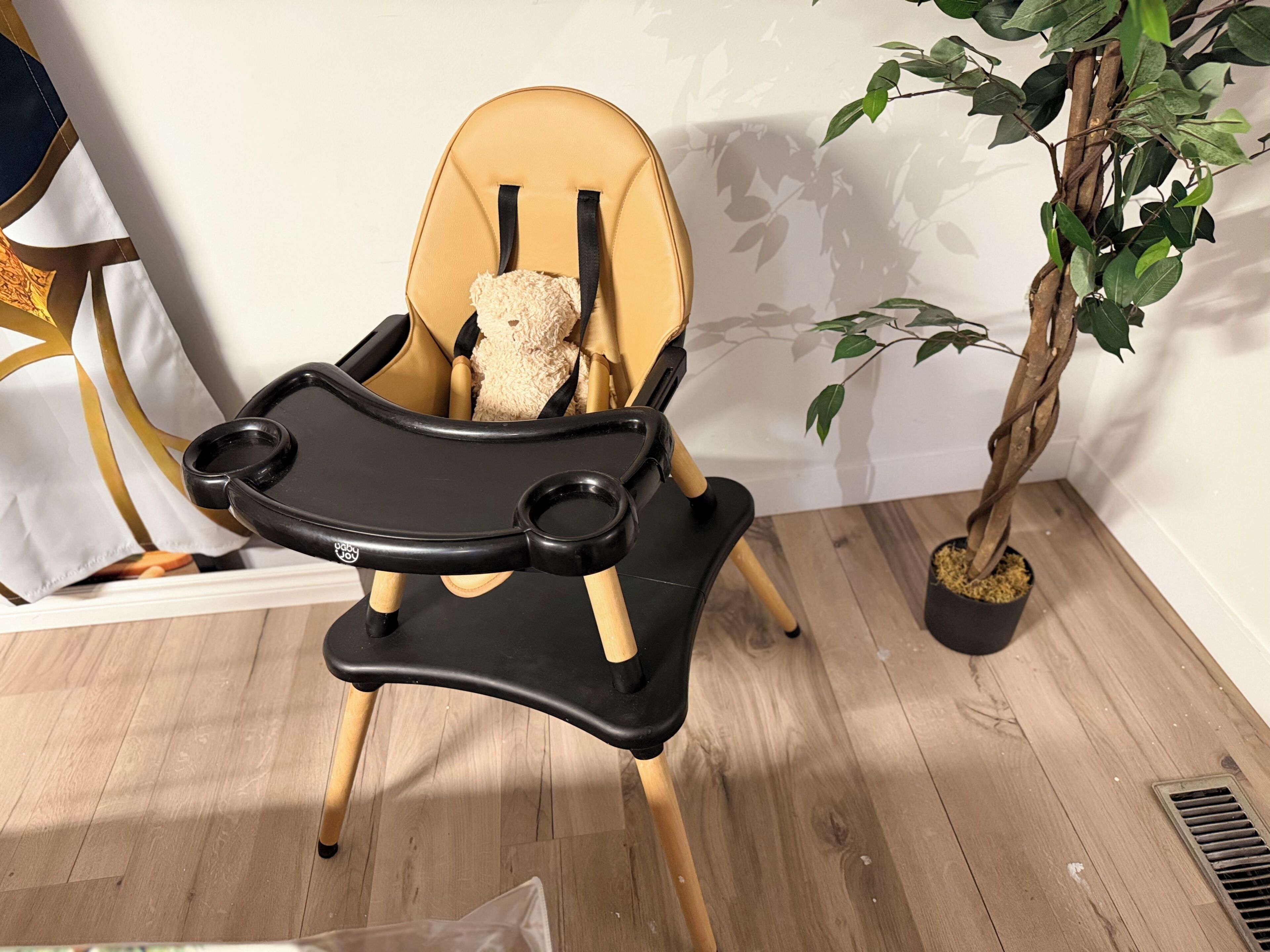 Syöttötuoli, jossa on pöytätaso, puujalat ja pehmustettu istuin.