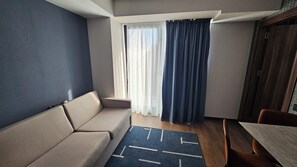 Ein kleiner, moderner Raum mit einer Couch, einem Esstisch und einem Vorhangfenster.