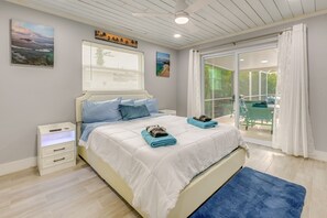 Ein Schlafzimmer mit einem Bett, einem Nachttisch, einem Fenster mit Jalousien und Blick ins Freie.