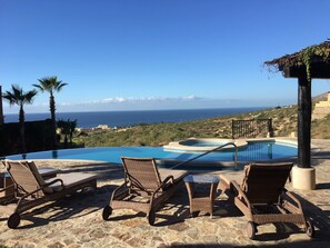 Una piscina infinita con sillones de descanso, un jacuzzi y vista al océano.