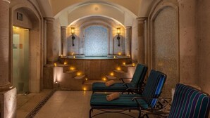 Uma área de spa com paredes de pedra, chão ladrilhado e duas cadeiras de descanso com toalhas.