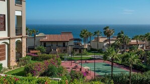 Resort com quadra de tênis, palmeiras e vista para o oceano.