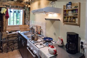 Une cuisine Ă©quipĂ©e dâune cuisiniĂšre, dâun Ă©vier et dâune machine Ă cafĂ©. Une fenĂȘtre offre une vue sur les arbres.