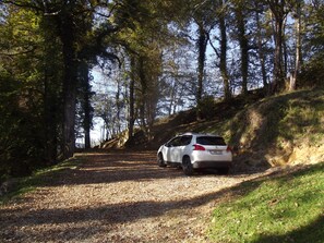 A white car parked on a gravel path in a wooded area.
