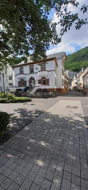 Ein gepflasterter Fußweg mit einem Gebäude, das eine Treppe und eine kleine Außenbestuhlung aufweist.