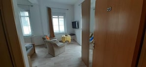 Ein Zimmer mit einer Couch, einem kleinen Tisch, einem Fernseher und einer Tür mit der Nummer 23.