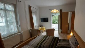 Ett sovrum med en säng, en stol, ett litet bord, en TV och en skjutdörr som leder ut till en balkong.