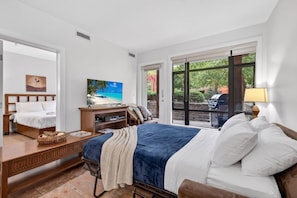 Une chambre à coucher comprenant un lit, un téléviseur, une commode en bois et une fen être donnant sur l’extérieur.