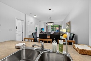 Une cuisine moderne dotée d’éviers en acier inoxydable, un coin repas avec une table et des chaises, et une vue sur l’extérieur.