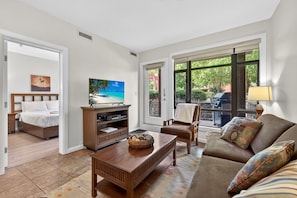 Un salon comprenant un canapé, une table basse, un téléviseur posé sur un meuble en bois, un fauteuil et un lit dans la pièce adjacente.