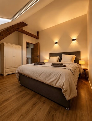 Ein Schlafzimmer mit einem großen Bett, Holzboden, einem Kleiderschrank und zwei Wandleuchten.