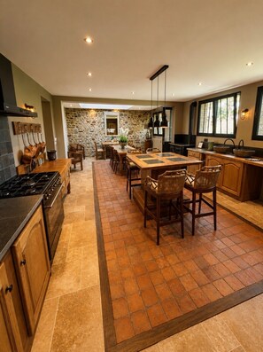 A modern kitchen with a central island, stone wall, and large windows. - Gite Chambord - 15 Pers. Mont-Saint-Michel Bay (Dragey-Ronthon)
