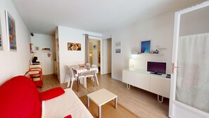 Ein Wohnzimmer mit einem roten Sofa, einem weißen Tisch und einem Fernseher auf einem weißen Schrank.