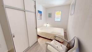 Ein Schlafzimmer mit Bett, Stuhl, Nachttisch, einem Fenster mit Vorhängen und einer Tür.