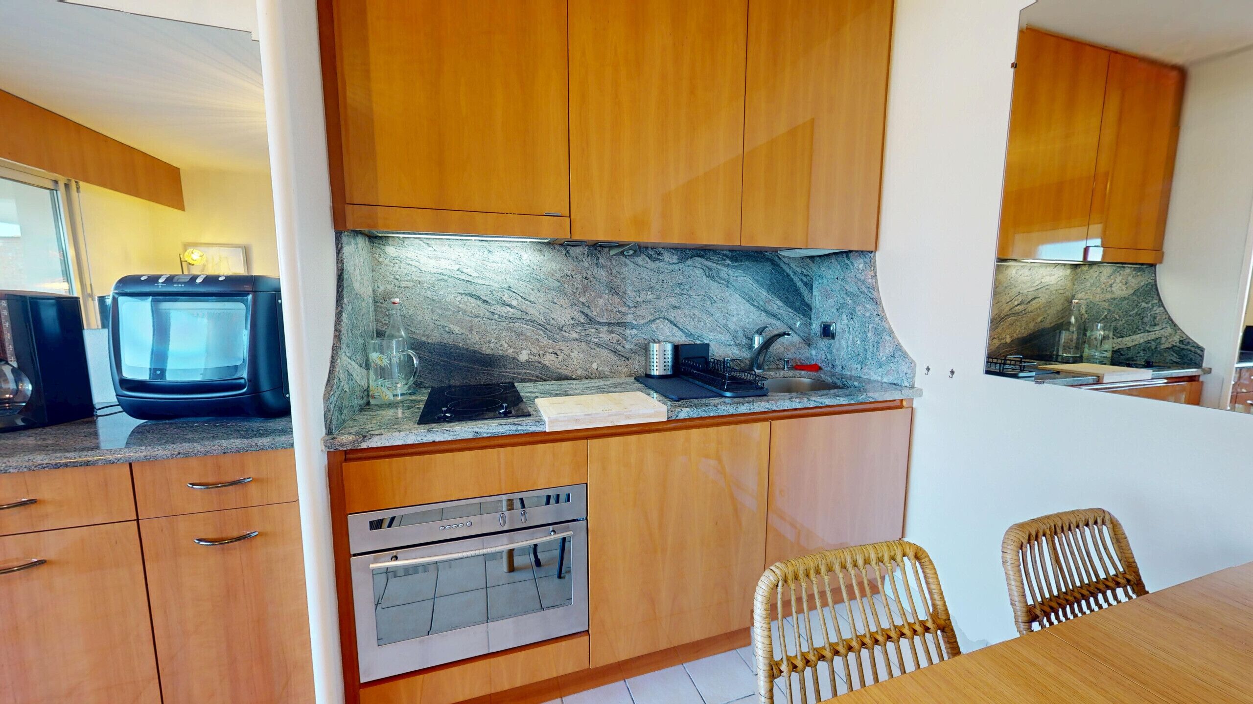 Una cucina compatta con mobili in legno, forno a incasso, microonde e un piano di lavoro in granito.