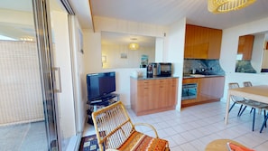 A compact living space with a kitchenette, a dining area, a television, and a wicker chair. - The Swordfish of Life - Garden Facing the Harbor (Saint-Gilles-Croix-de-Vie)