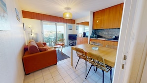 Un salon moderne comprenant un canapé, une table à manger et des chaises, une cuisine avec des meubles en bois et une grande fenêtre donnant sur un paysage.