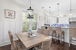 A modern kitchen with white cabinetry, a wooden dining table, wicker chairs, pendant lighting, and a view of the outdoors. - ☀️Jaybird Bungalow-Bikes-Community Pool☀️ (Santa Rosa Beach)